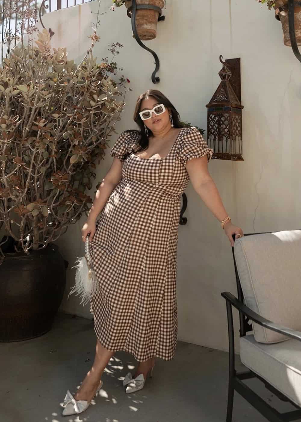 a woman wearing a brown gingham midi dress with white bow tie pumps