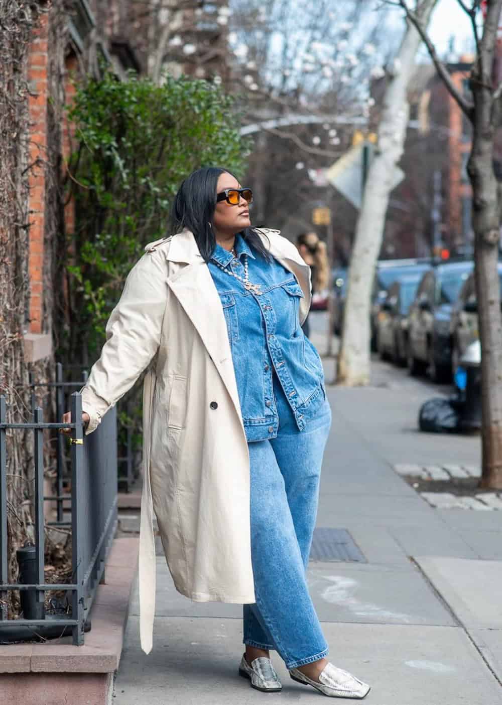 a woman wearing a plus size thanksgiving outfit featuring a denim set and an ivory trench coat with snakeskin loafers