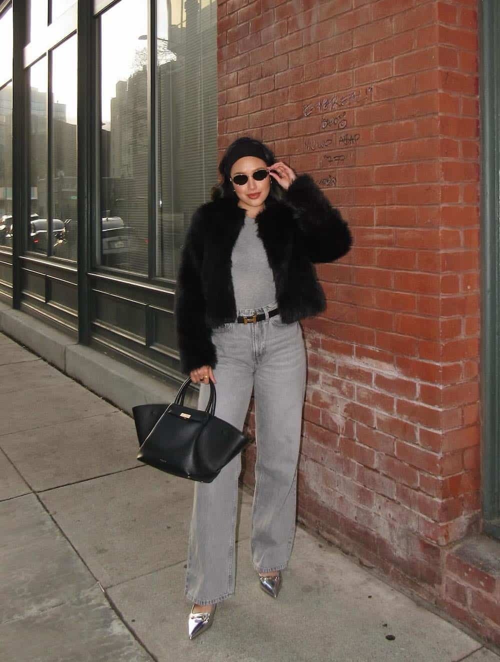 a winter concert outfit featuring grey wide-leg jeans, a grey tank, silver pumps, and a faux fur black coat
