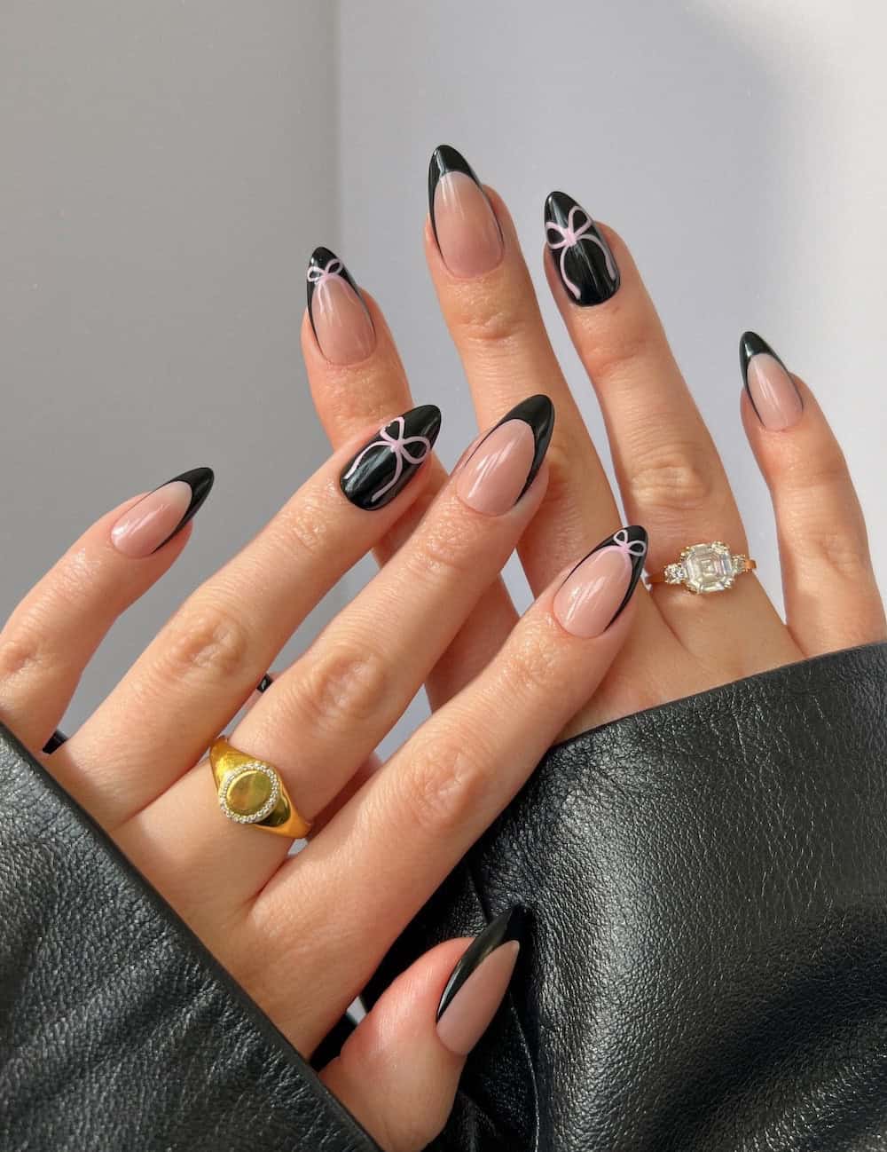 nude almond nails with black french tips and black accent nails with pink bow details