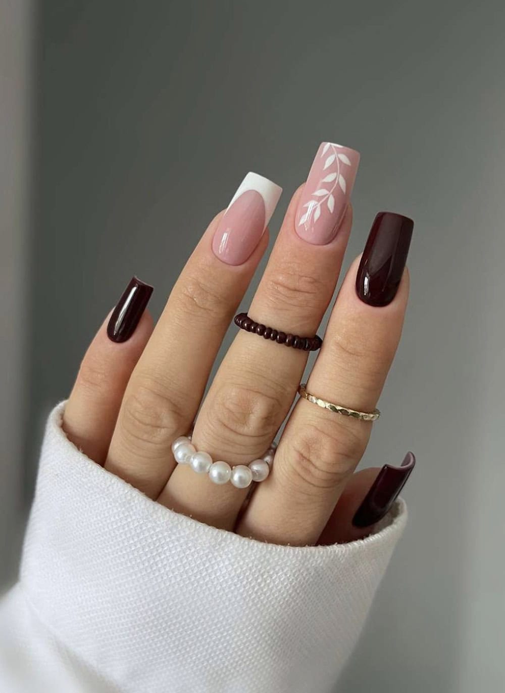 dark brown square nails with nude pink accent nails featuring white tips and leaf art