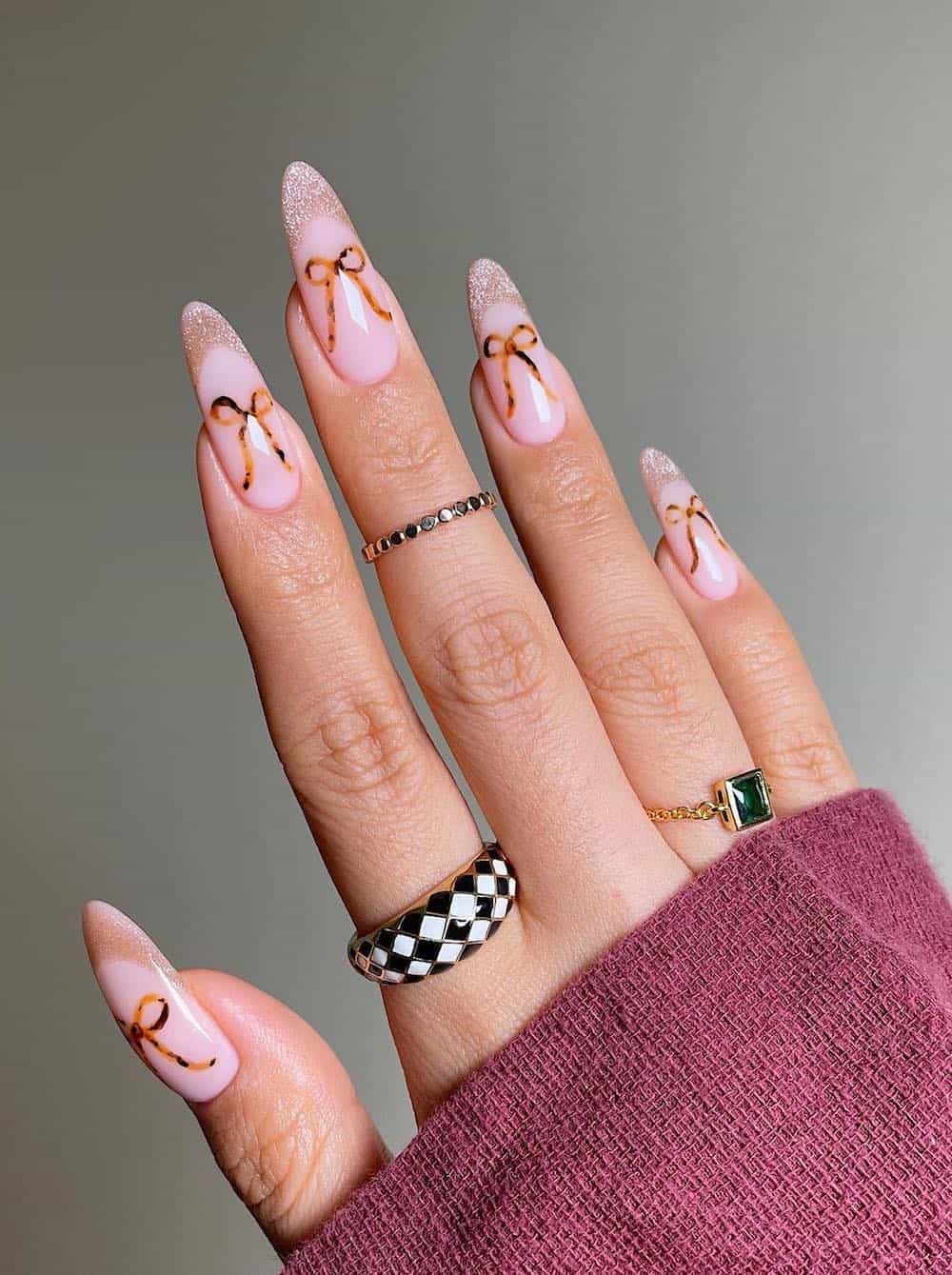 long pink nude almond nails with shimmering tips and brown bows