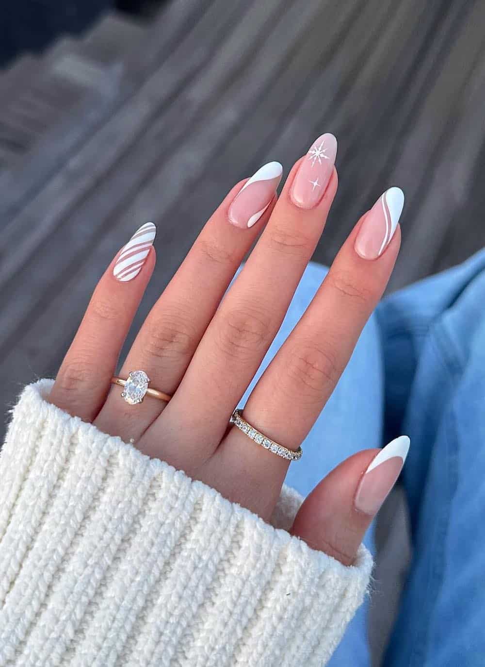 nude pink almond nails with white swirls, stripes, snowflakes, and tips