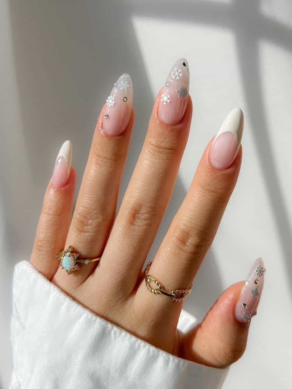 long milky white almond nails with snowflake embellishments and white tip accents