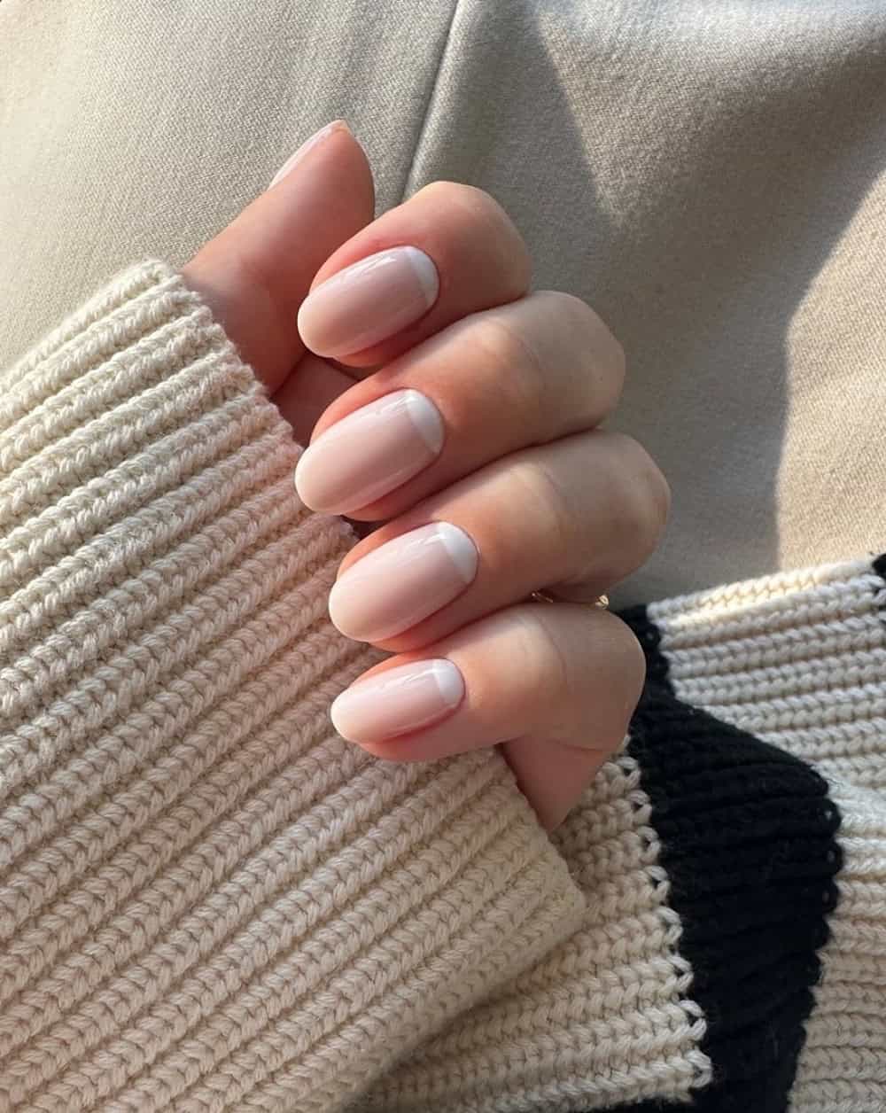 short round nails with nude polish and white reverse french tips