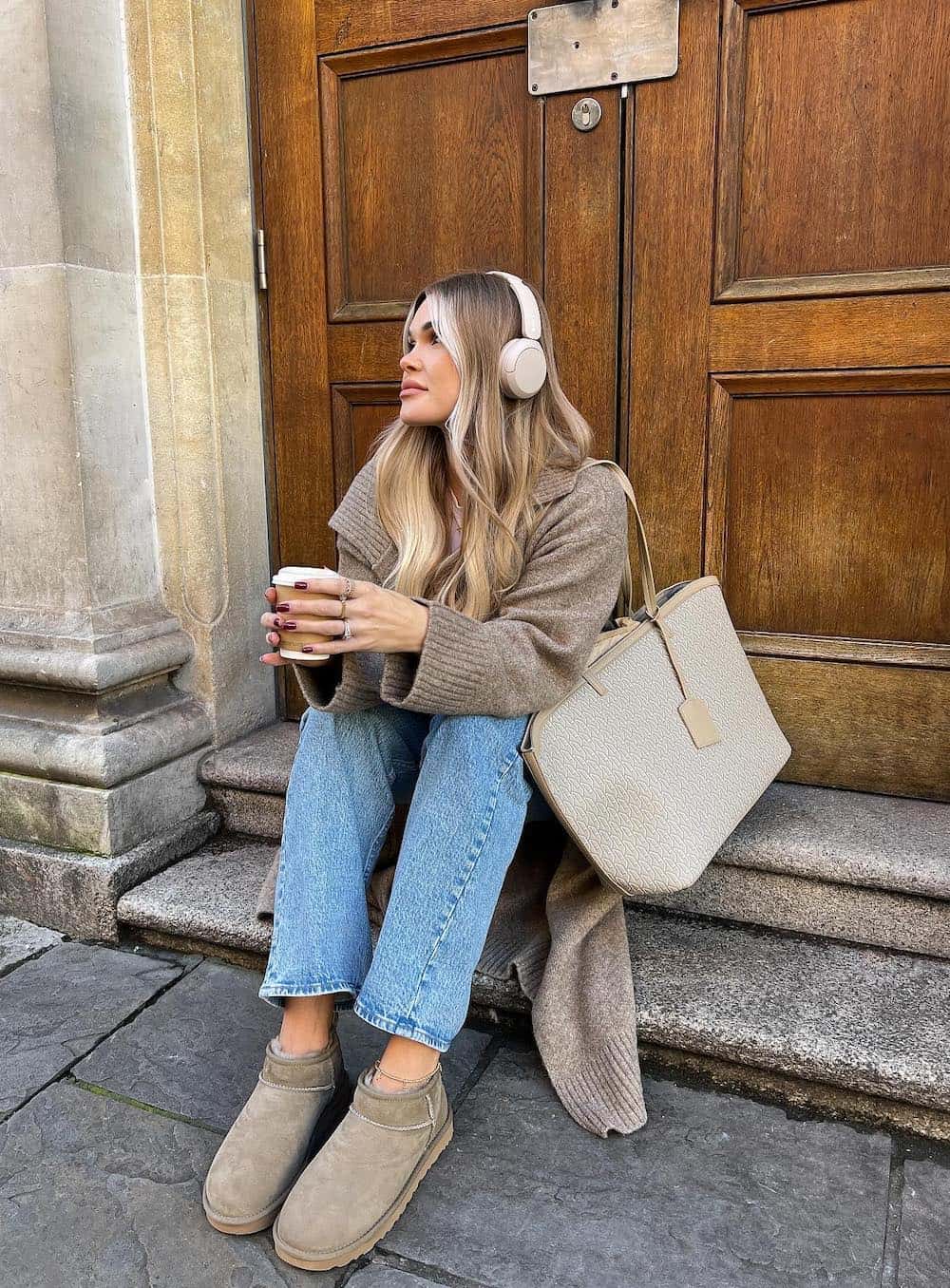 Woman wearing jeans, Ugg boots and a tan sweater.