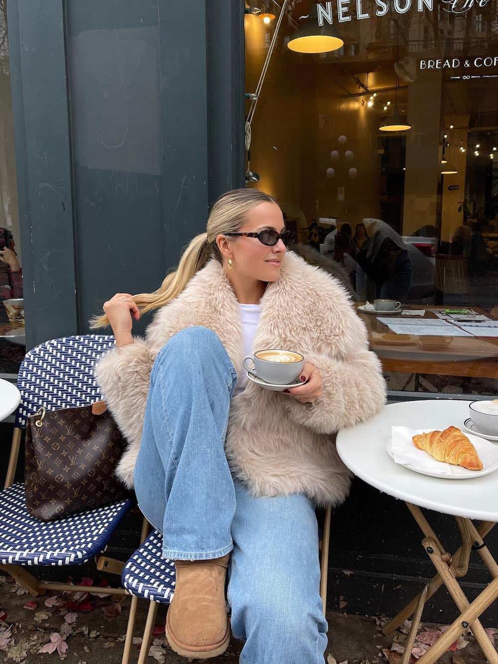 Woman wearing jeans, a white t-shirt, a faux fur jacket and Ugg boots.