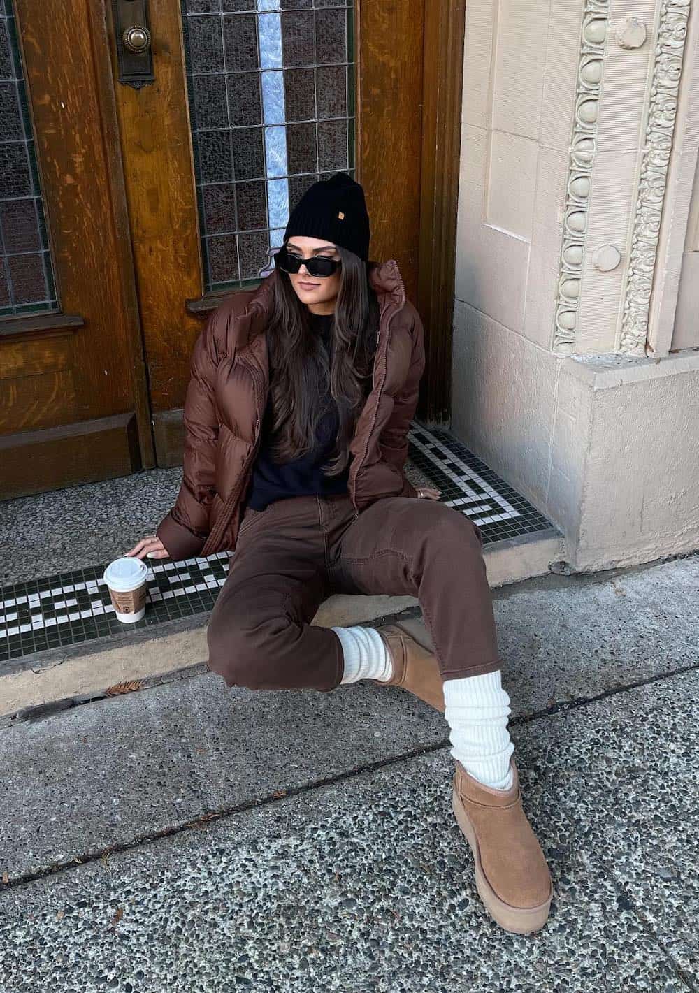 Woman wearing brown skinny jeans, Ugg boots, tall socks and a brown puffer jacket.