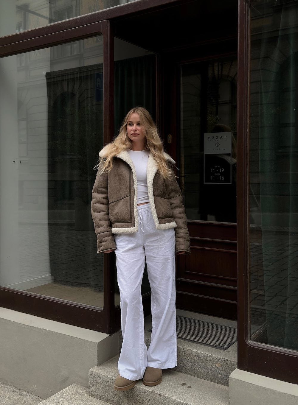 Woman wearing white pants, a white t-shirt, a faux fur coat and Ugg boots.