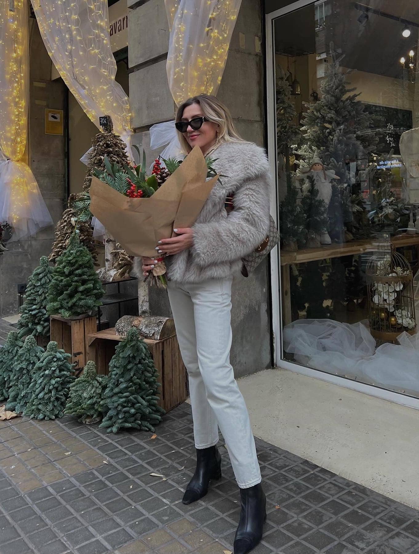 Woman wearing white jeans with black booties and a light grey faux fur jacket.