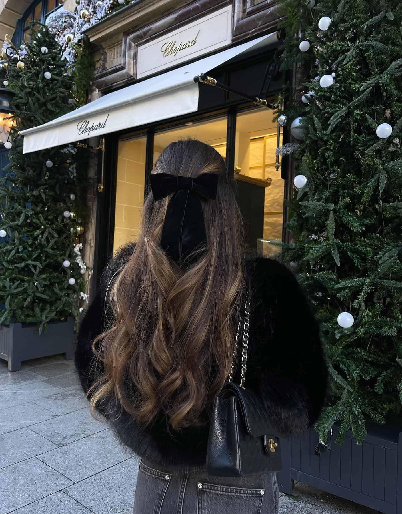 Woman wearing black jeans, a black eyelash sweater and a black velvet bow in her hair.