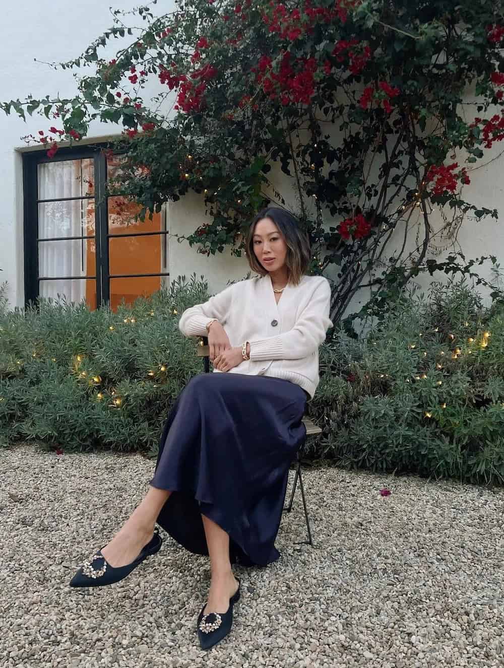 Woman wearing a navy skirt with a white cardigan and navy ballet flats.