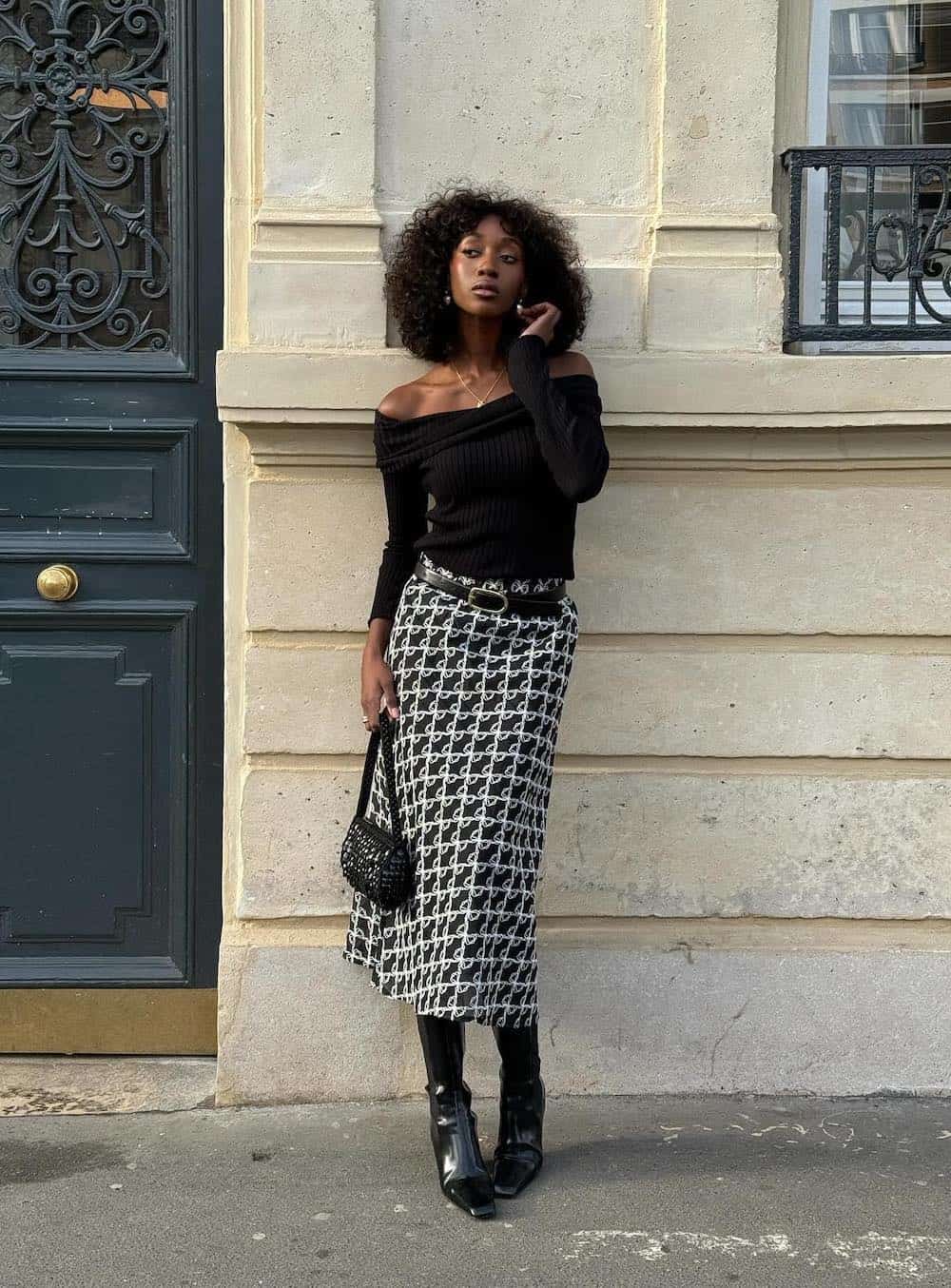 Woman wearing a black and white geometric print midi skirt with a black off the shoulder top and black boots.