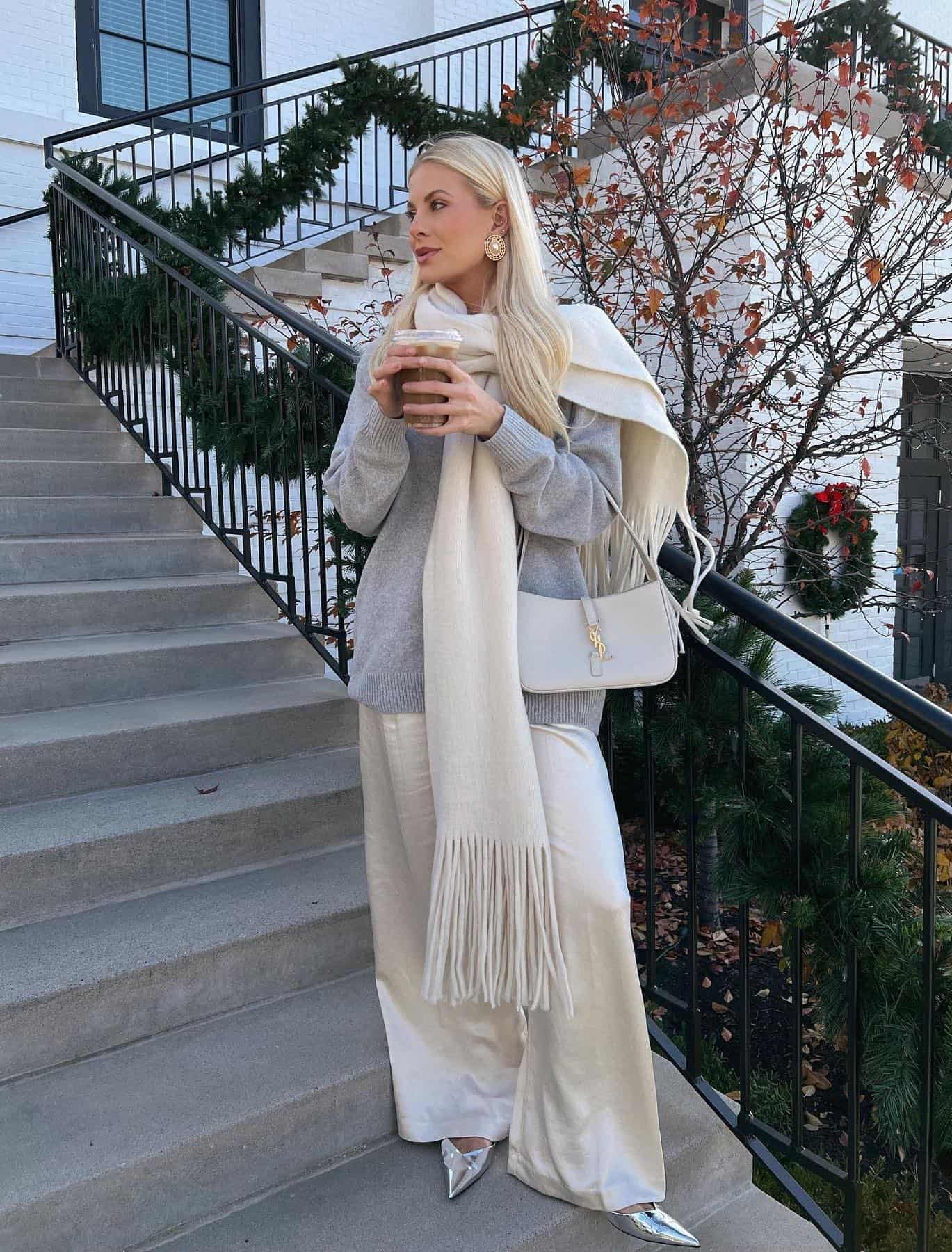 Woman wearing white silk pants, a grey sweater, silver pumps and a white scarf.