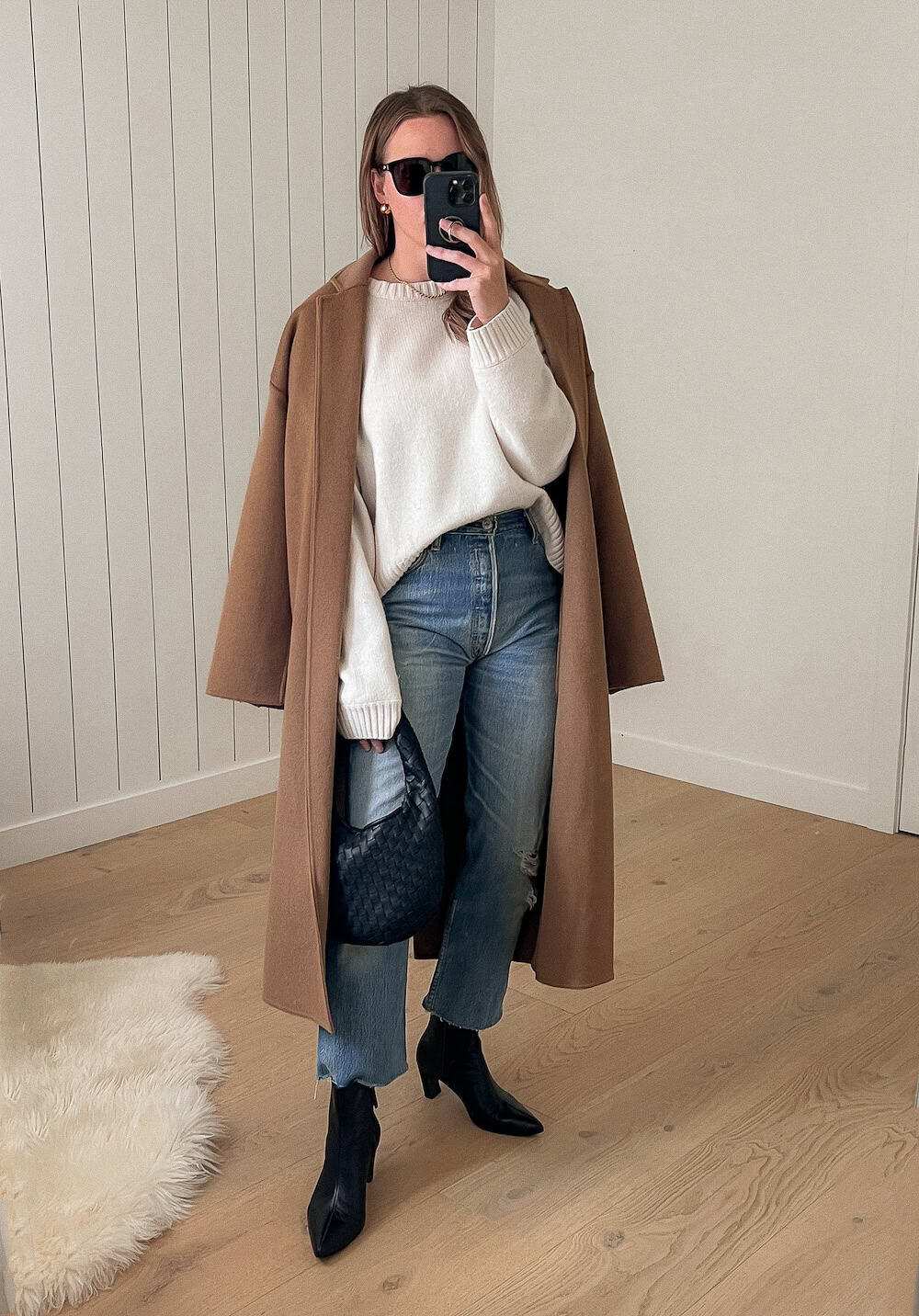 Christal wearing jeans, black booties, a white sweater and a camel colored long coat.