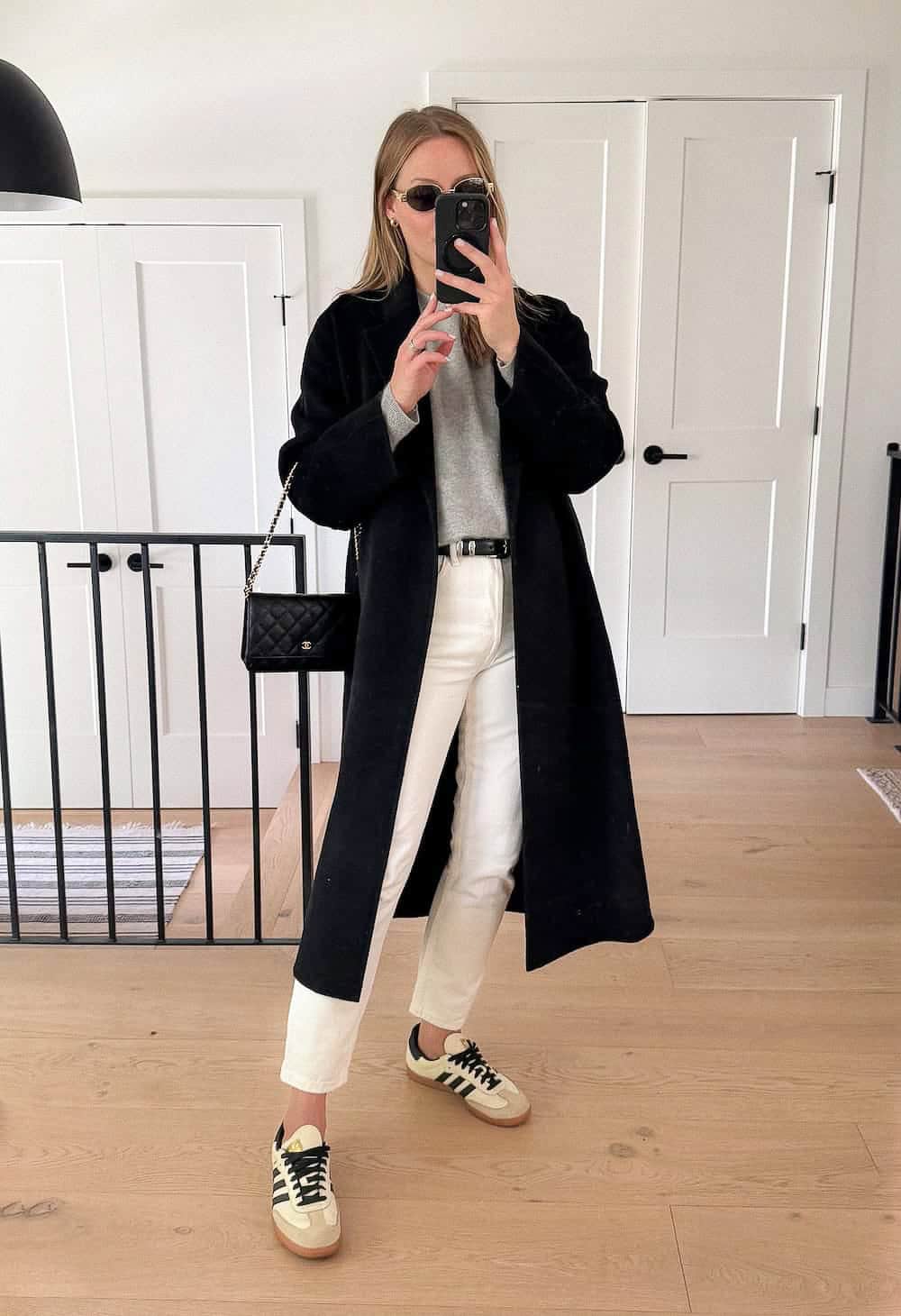 Christal wearing white jeans, sneakers, a grey sweater and a long black coat.