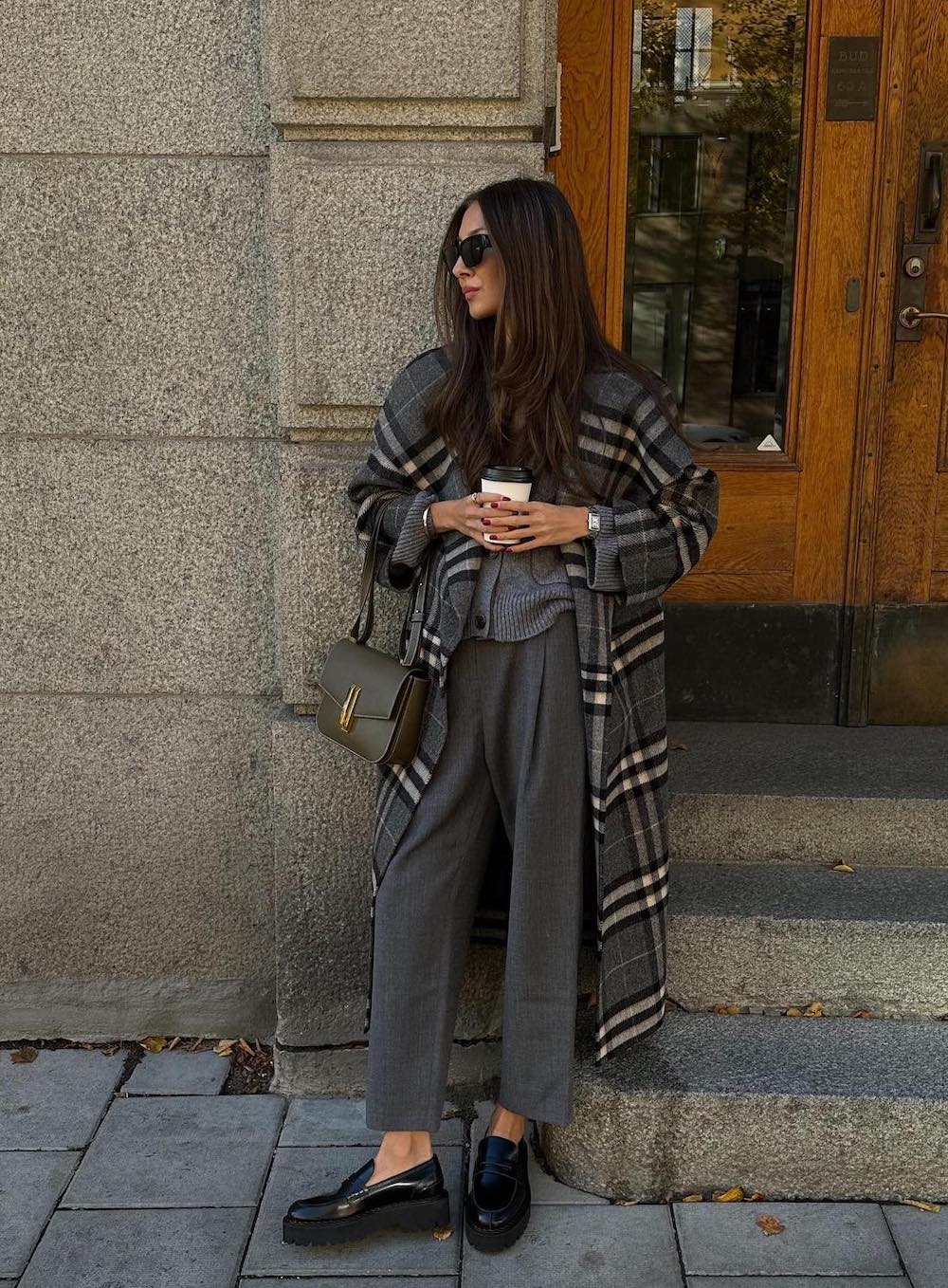 Woman wearing trousers and a cardigan with a long plaid coat.