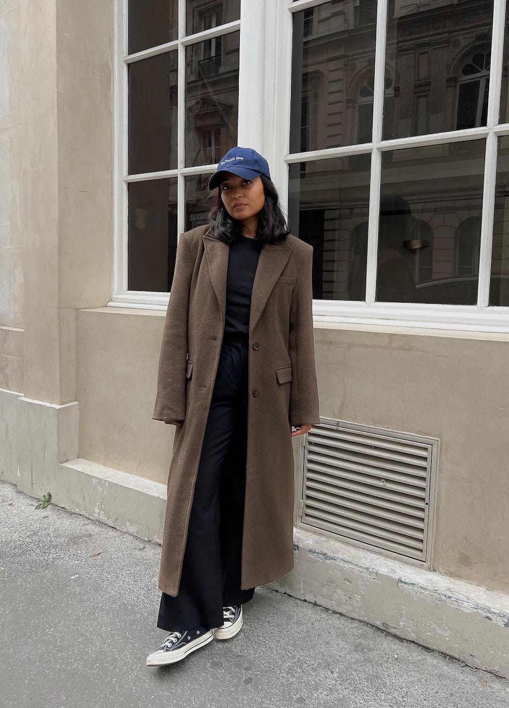 Woman wearing black wide leg pants with sneakers and a long brown coat.