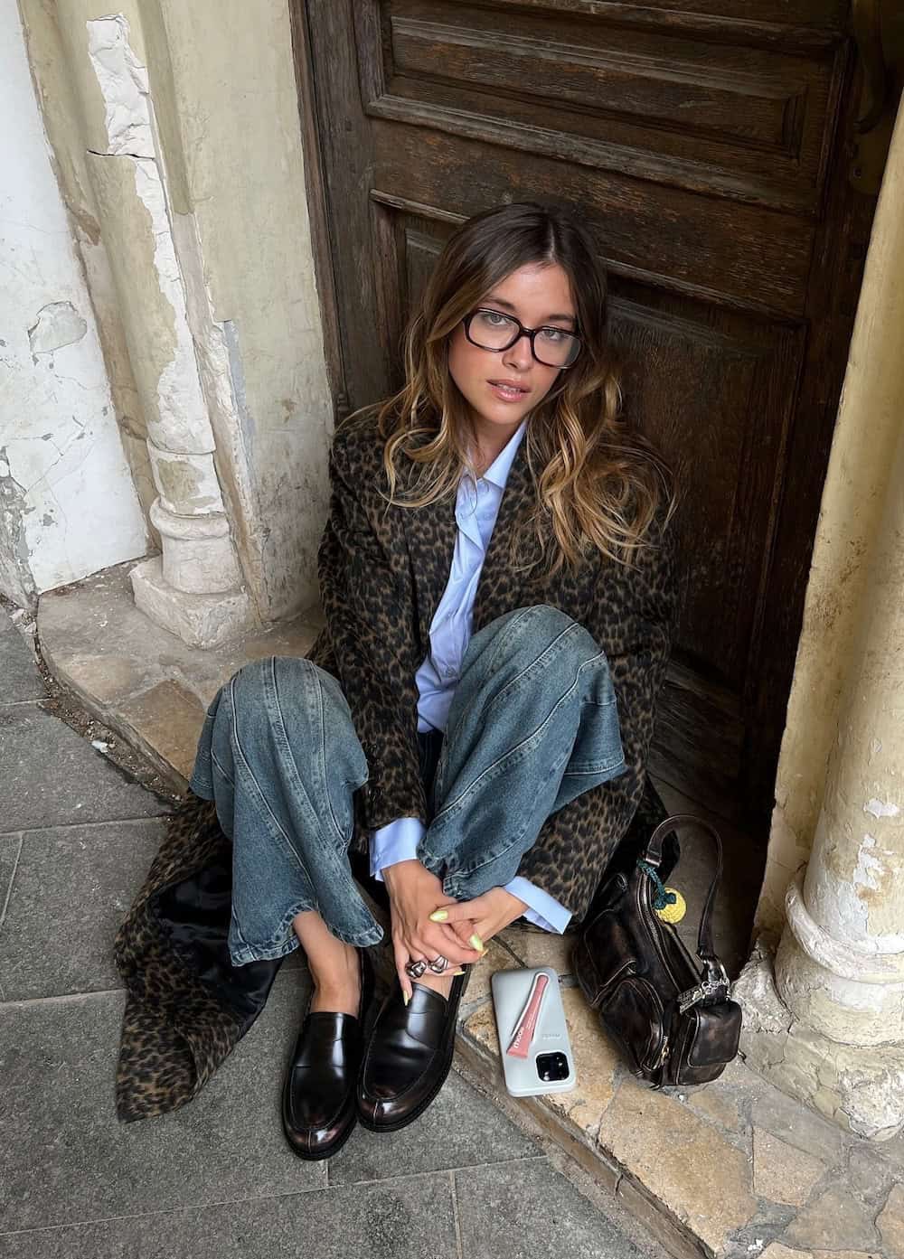 Woman wearing jeans, a button down and a long animal print coat.