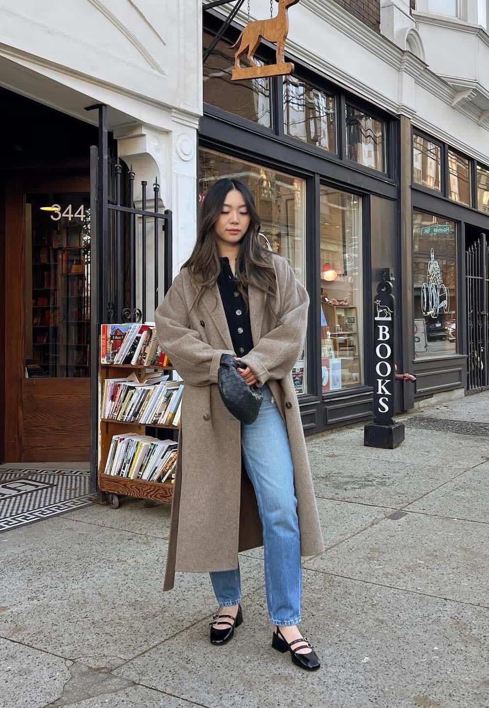 Woman wearing jeans, a black button down, Mary Jane flats and a grey long coat.