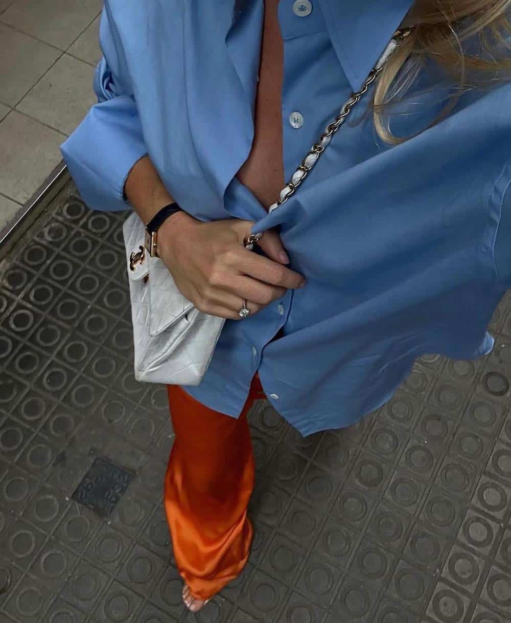 Christal wearing orange silk pants with a blue button down and a white Chanel bag.