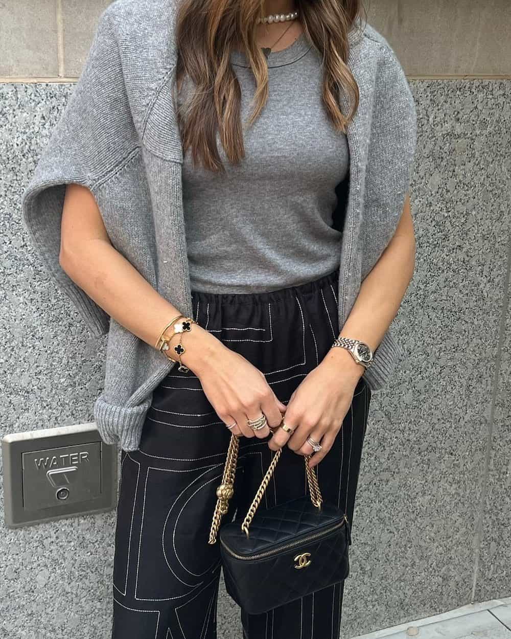 Woman wearing silk pants with a geometric pattern and a grey knit top and sweater.