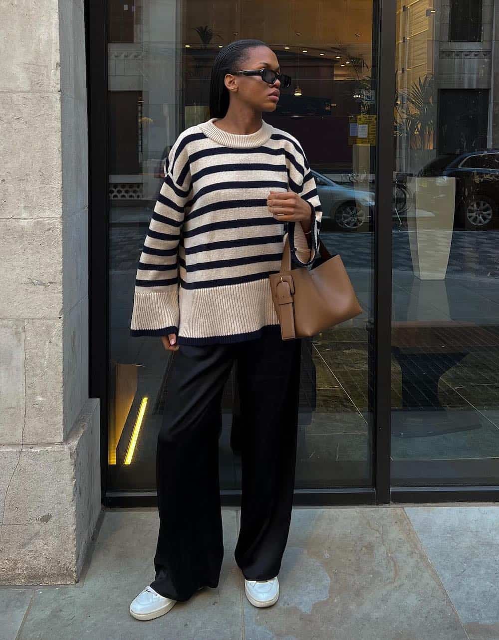 Woman wearing black trousers with a black and cream oversized sweater and white sneakers.