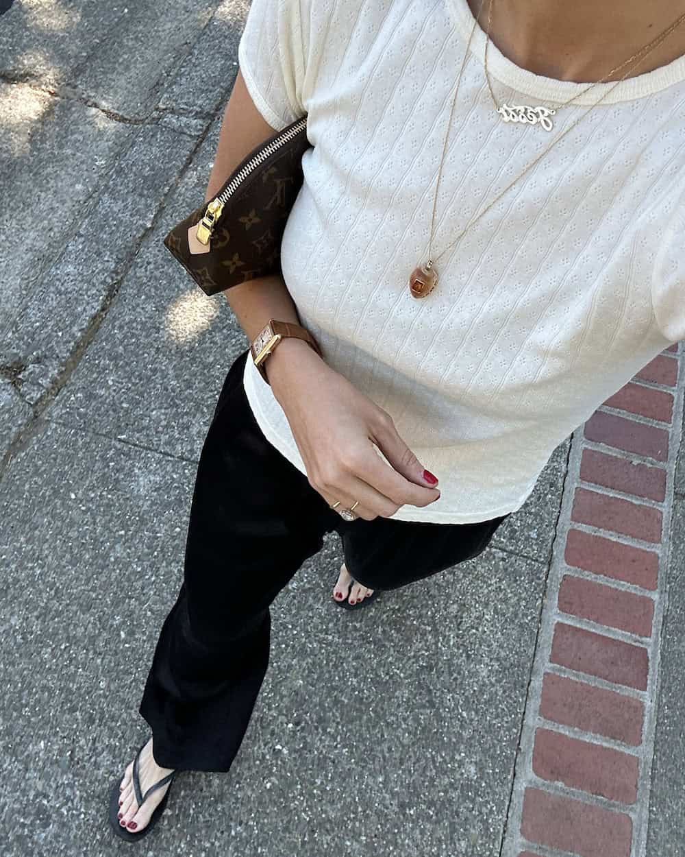 Woman wearing black silk pants with a white knit top and flip flops.