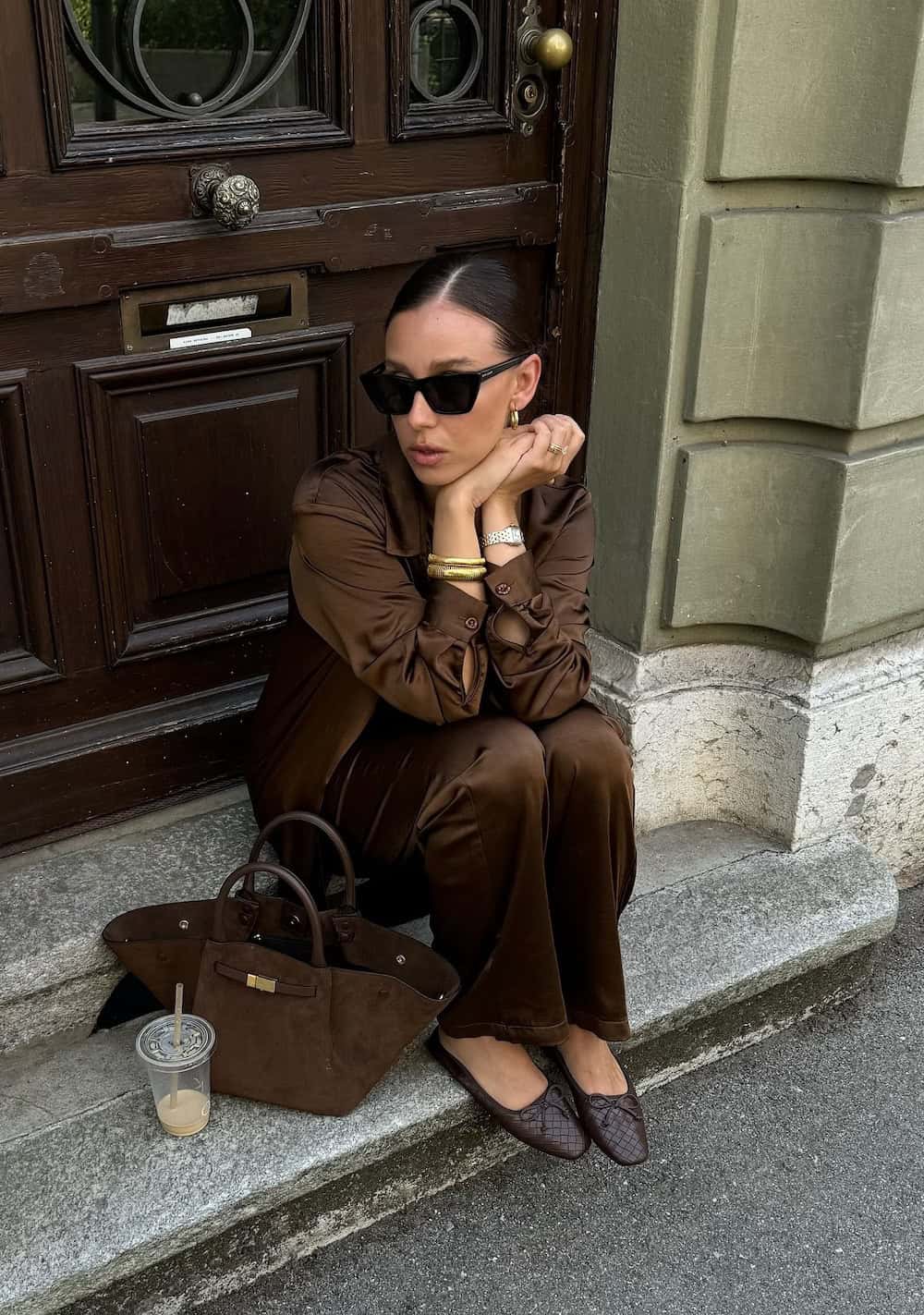 Woman wearing a coordinating brown silk pant and blouse set with brown ballet flats.