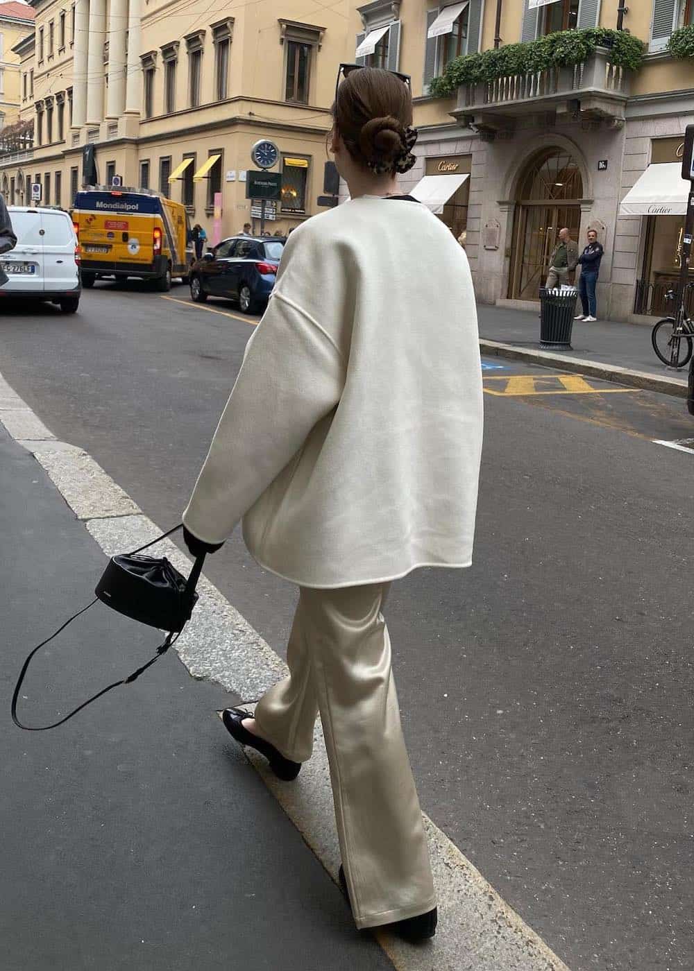 Woman wearing white silk pants with an oversized white sweater and black ballet flats.