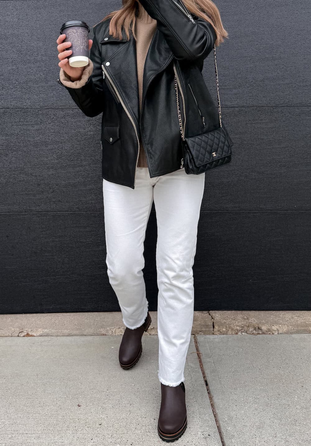 a woman wearing white straight leg jeans, a beige turtleneck sweater, a black leather jacket, and black chelsea boots