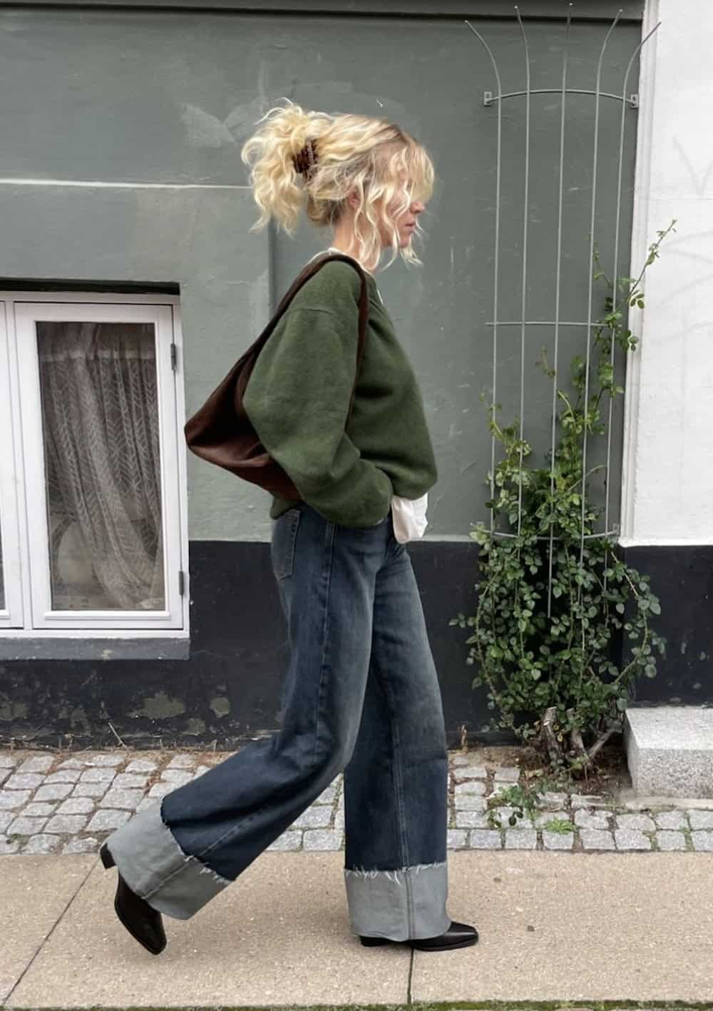 a woman wearing black chelsea boots, wide lg blue jeans, and a dark green sweater