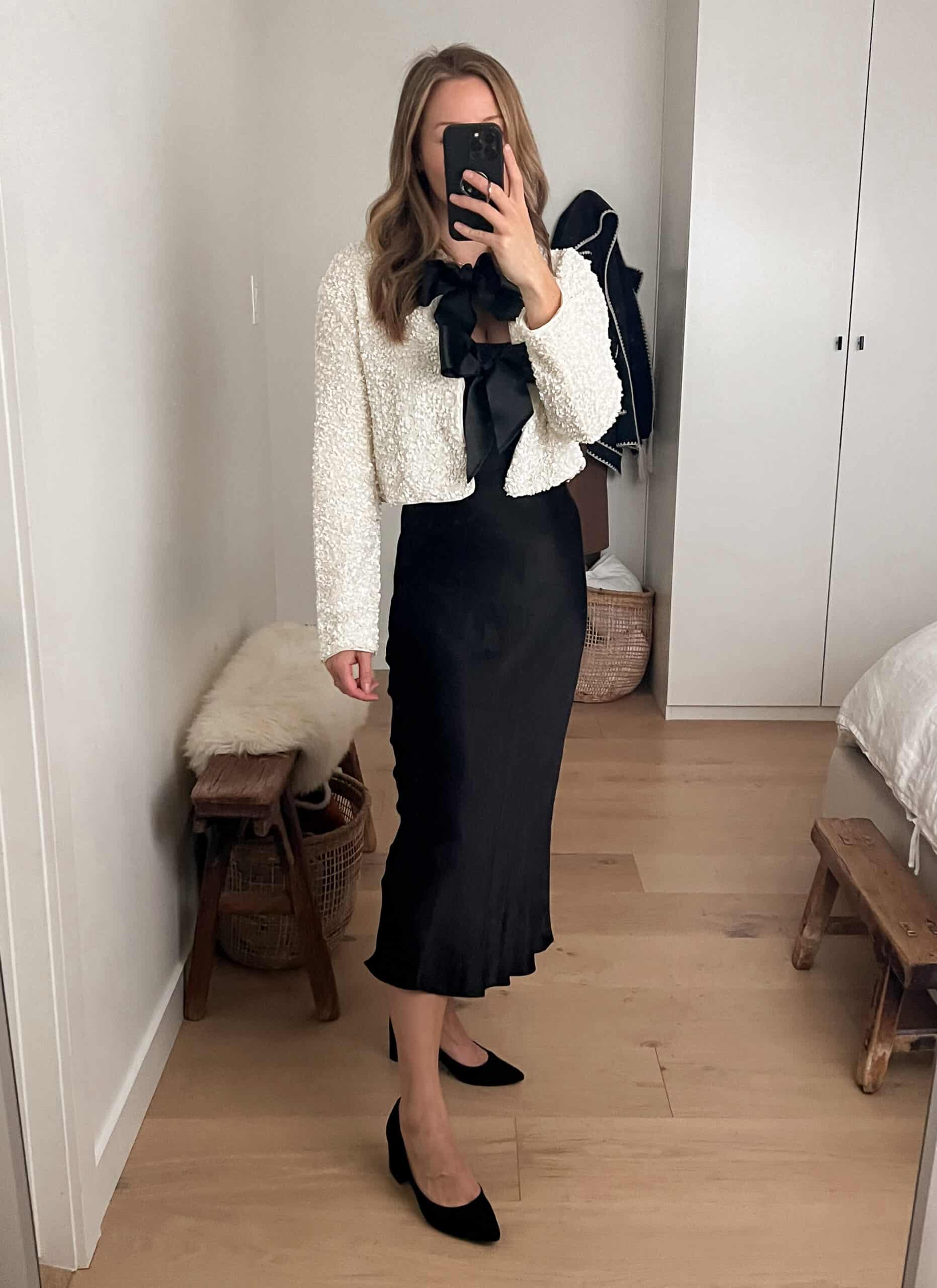 Christal wearing a black satin dress with a white sweater with black bows and black pumps.