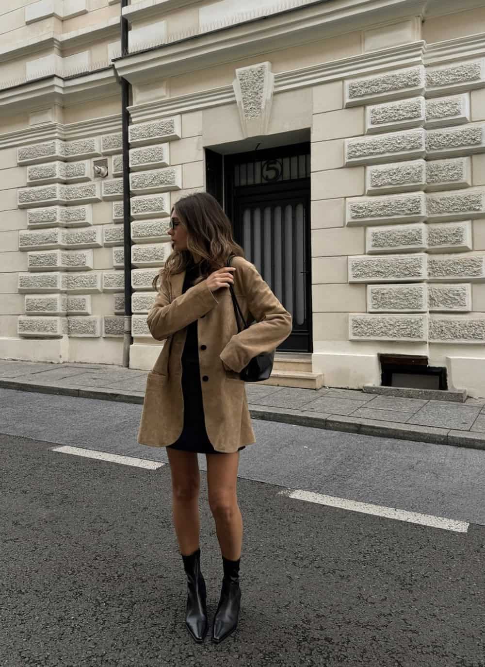 a woman wearing a little black dress, a brown suede jacket, and pointed black leather chelsea boots