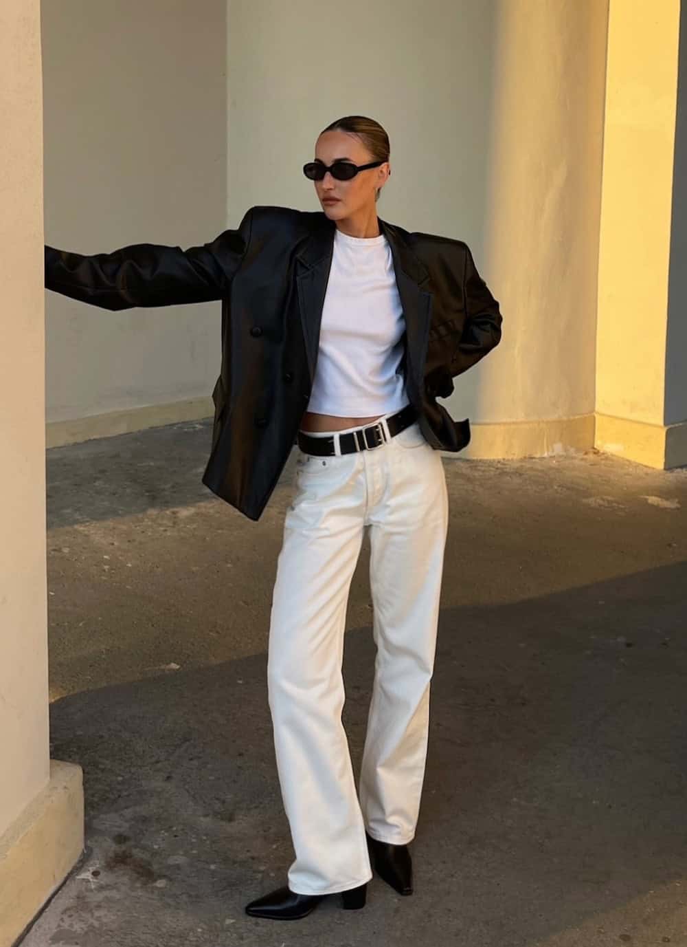 a woman wearing a white tee, white wide leg jeans, a black leather blazer, and black chelsea boots