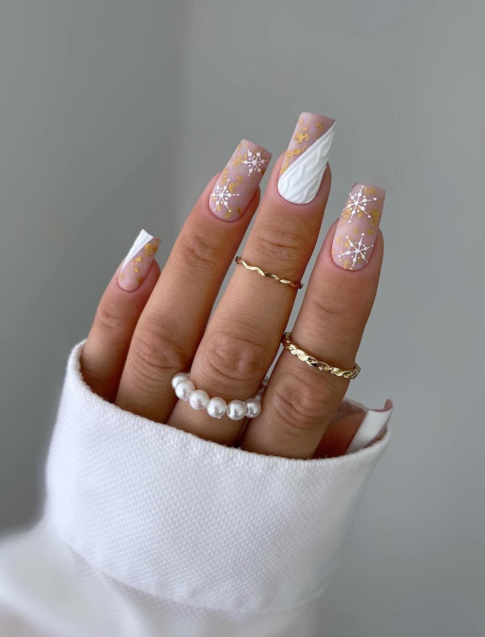 long square nails featuring beige base polish with white accents, snowflakes, and gold details