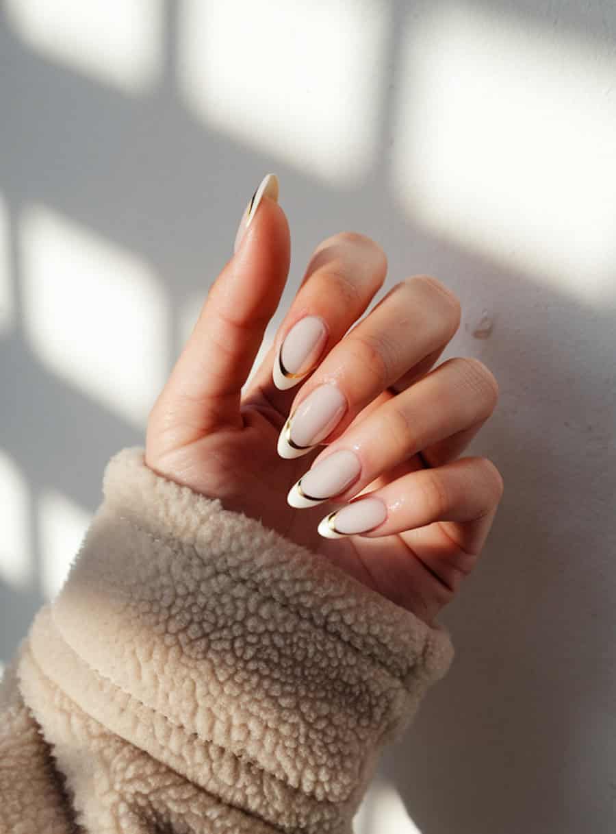 long glossy nude almond nails with white tips and gold bands