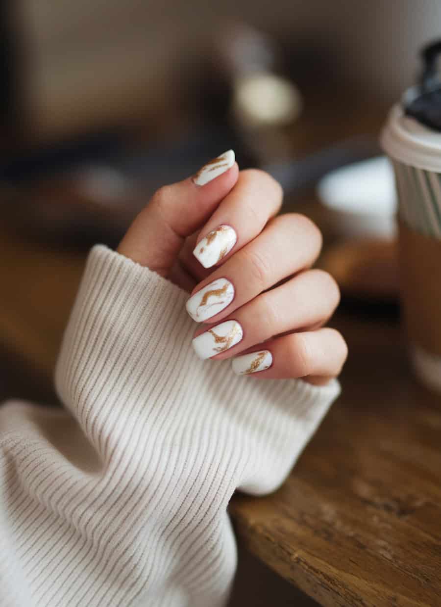 short square nails with white nail polish and gold marbling