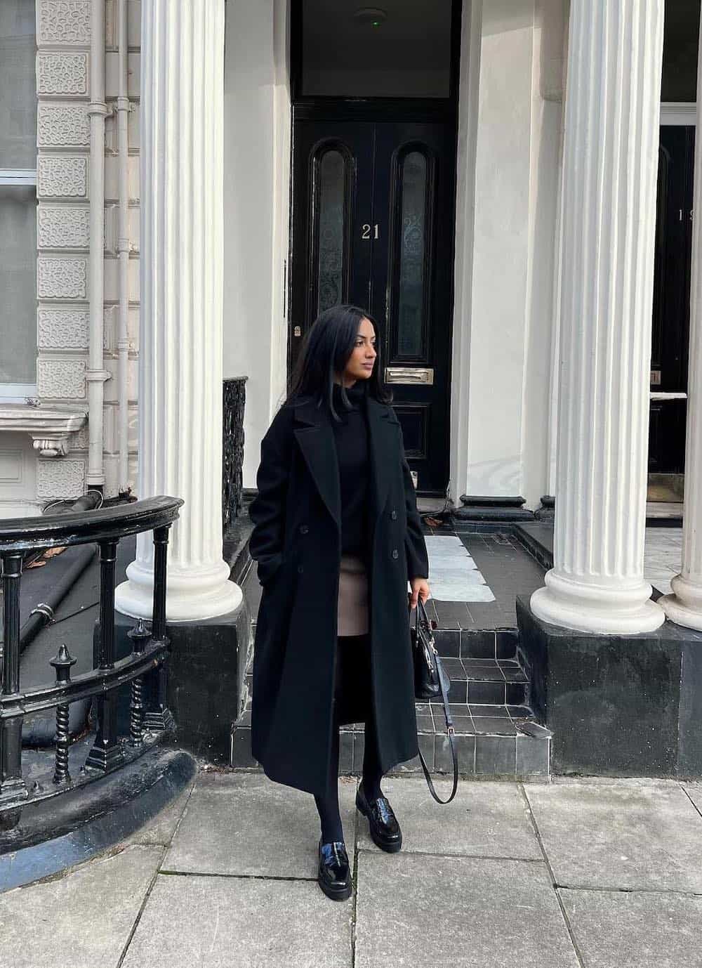 Woman wearing loafers with black tights, a brown skirt and a black coat.