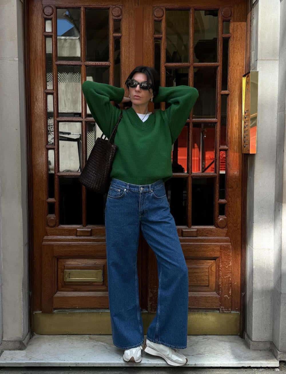 Woman wearing jeans with New Balance sneakers and a green sweater.