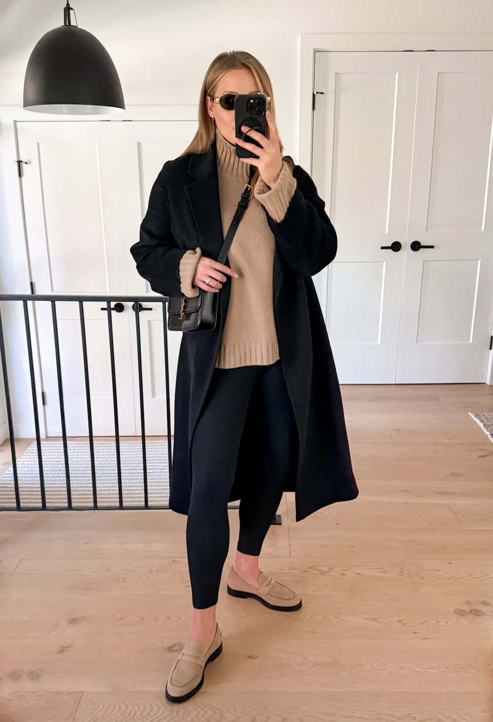 a woman wearing black leggings, a beige sweater, a black wool coat, and beige suede loafers