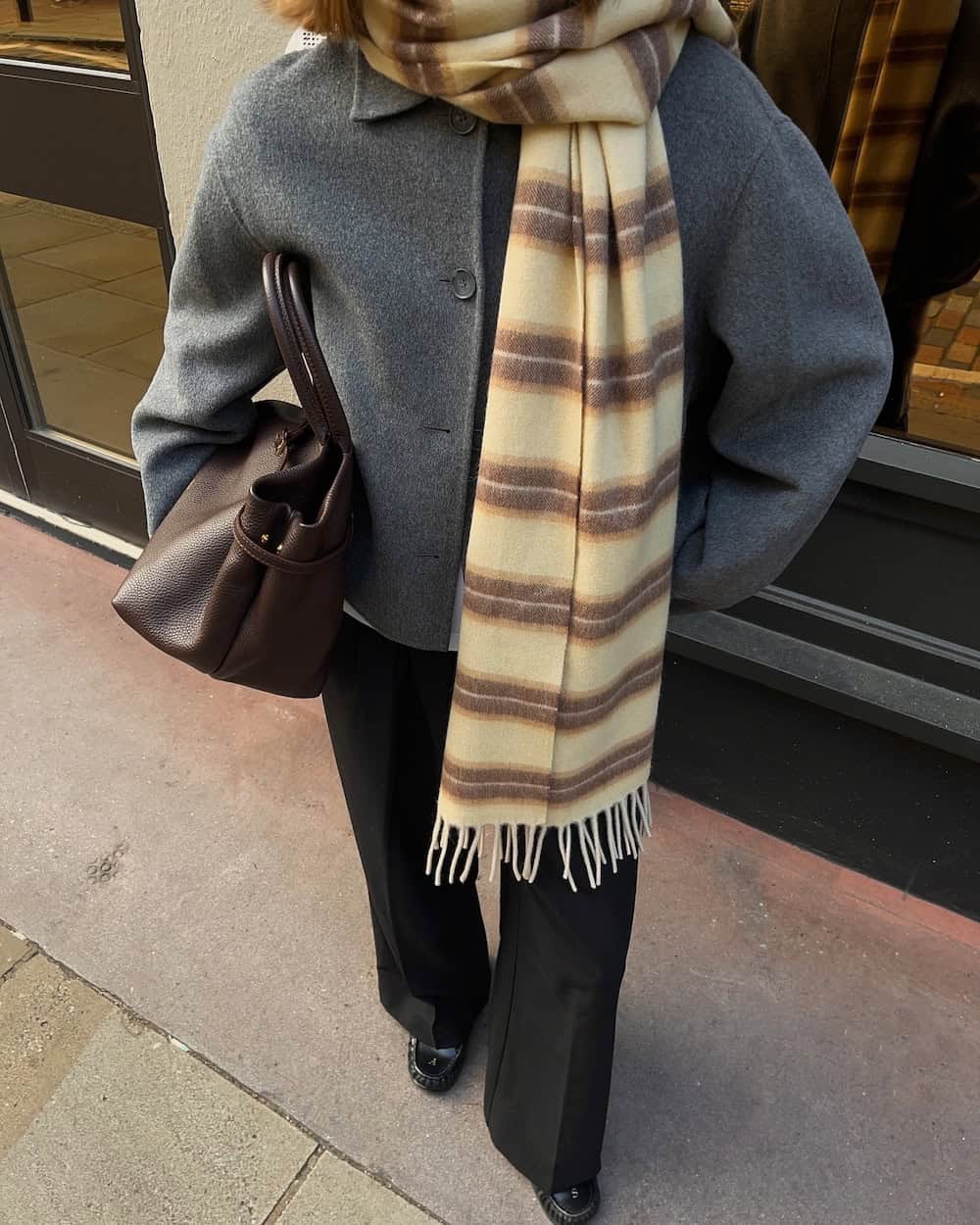 a woman wearing grey sweater coat, black trousers, and brown and beige striped scarf