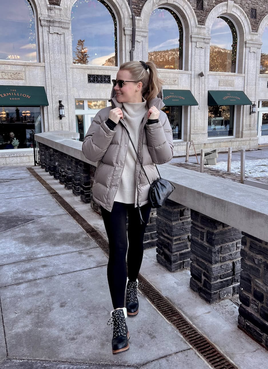 a woman wearing black leggings, a soft beige turtleneck, a puffer coat, and black winter boots