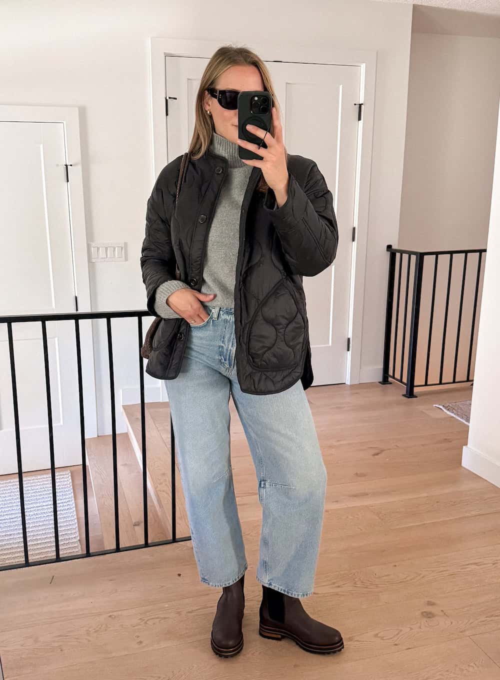 a woman wearing blue jeans, a grey turtleneck, a black quilted coat, and black chelsea boots
