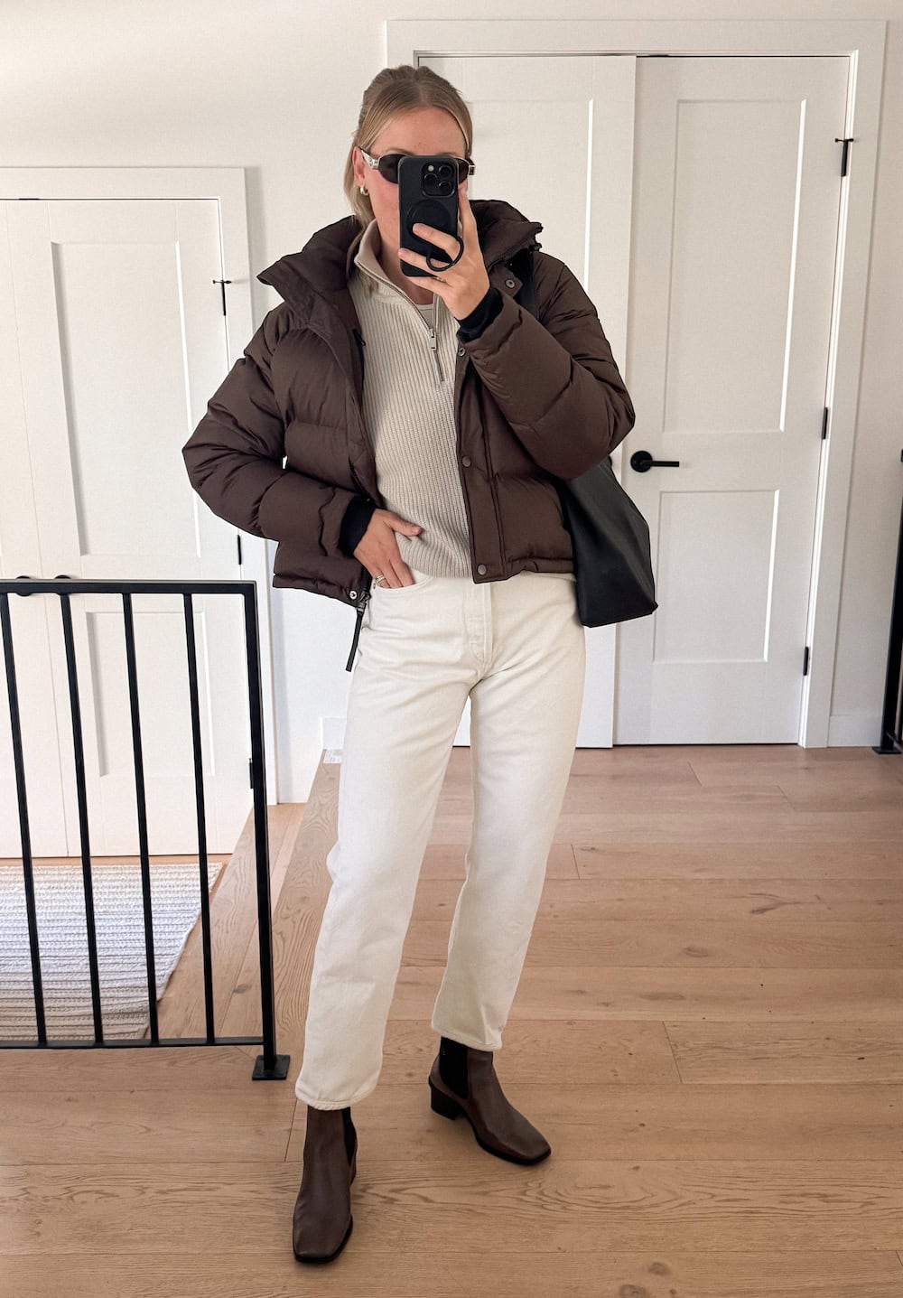 a woman wearing white jeans, a light beige half zip, a brown puffer coat, and brown boots