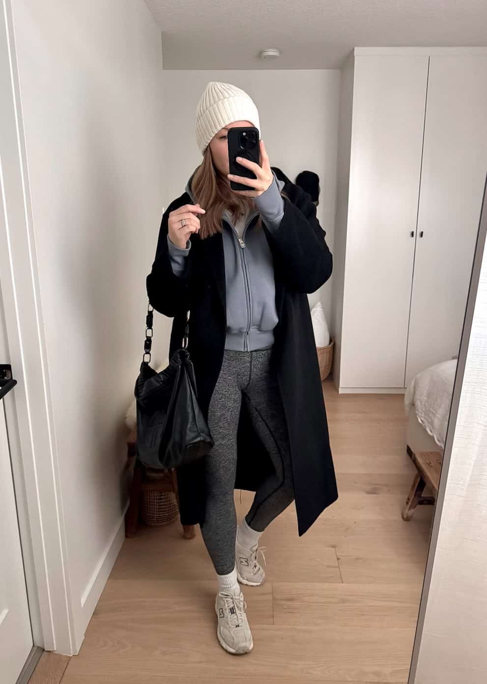 a woman wearing grey leggings, a blue hoodie, a long black coat, and athletic sneakers