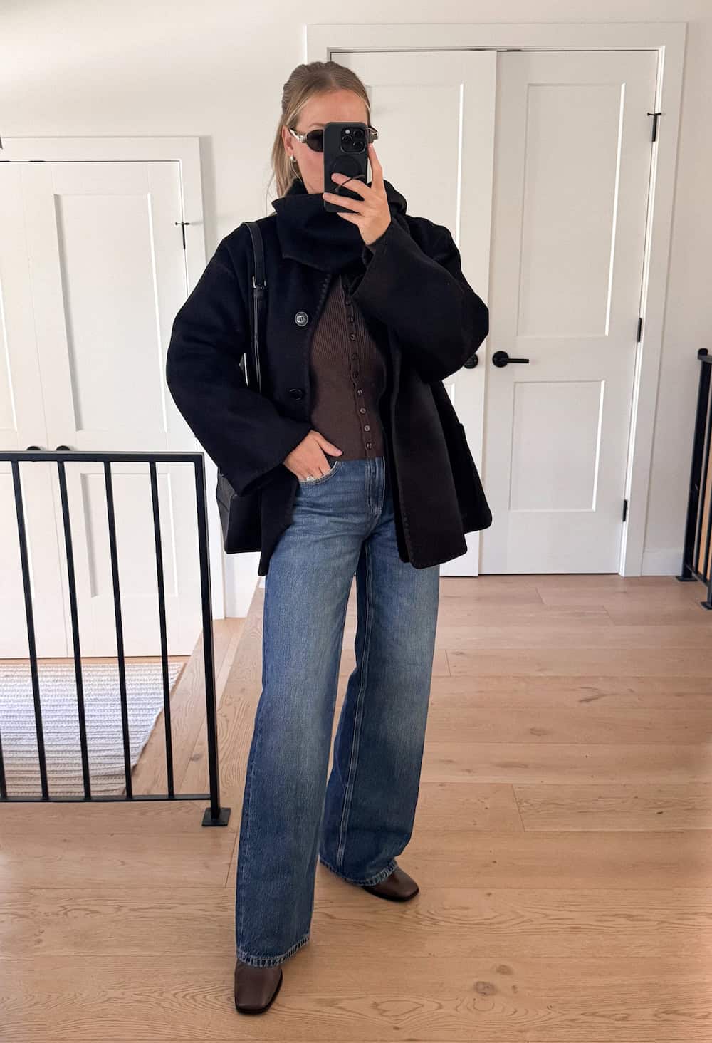 a woman wearing blue jeans, a brown cardigan, a black scarf jacket, and boots