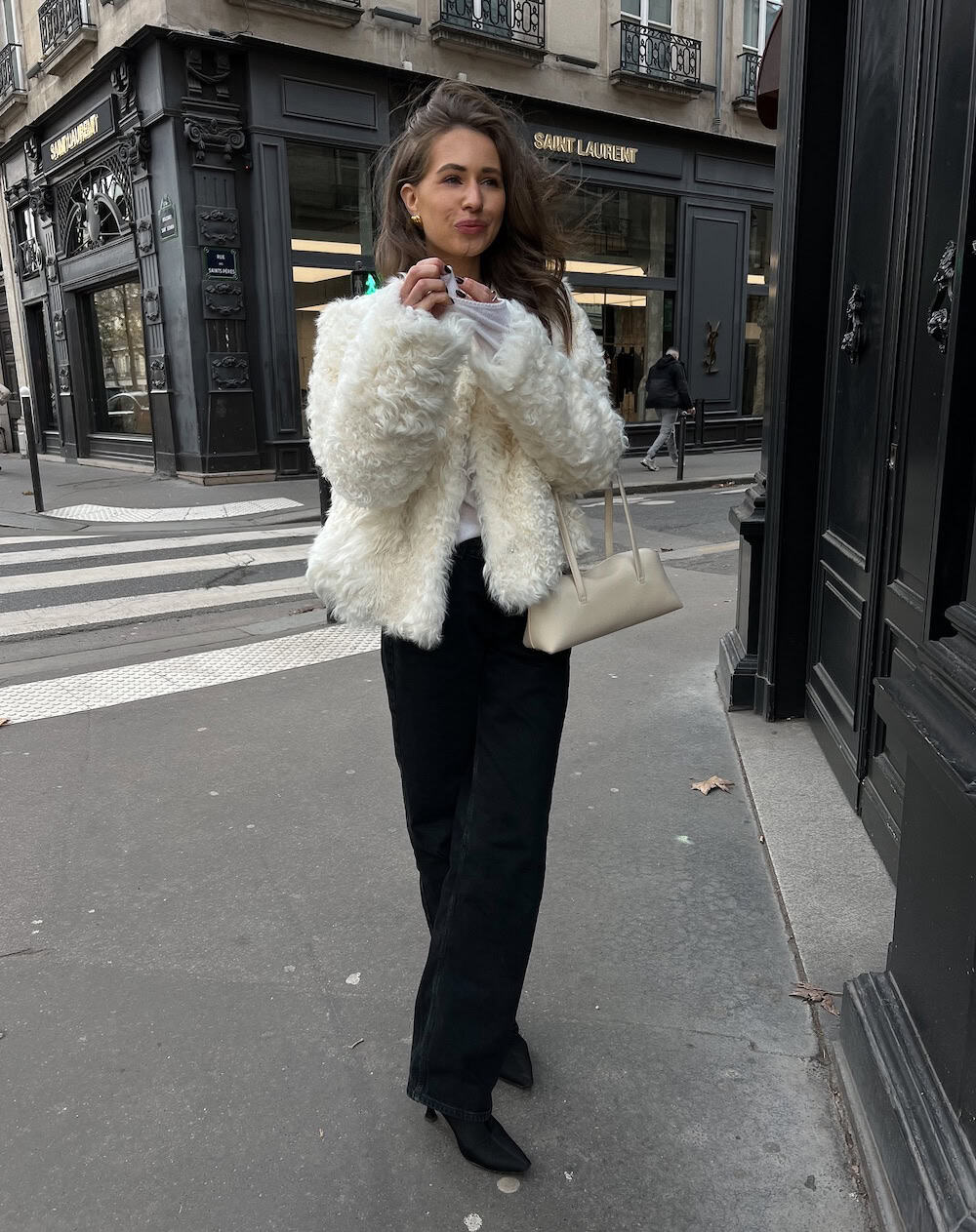 a woman wearing black jeans, a white faux fur coat, and heeled boots