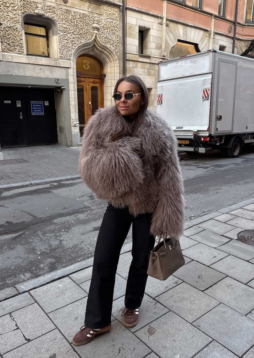 a woman wearing black pants, a faux fur coat, and brown sneakers