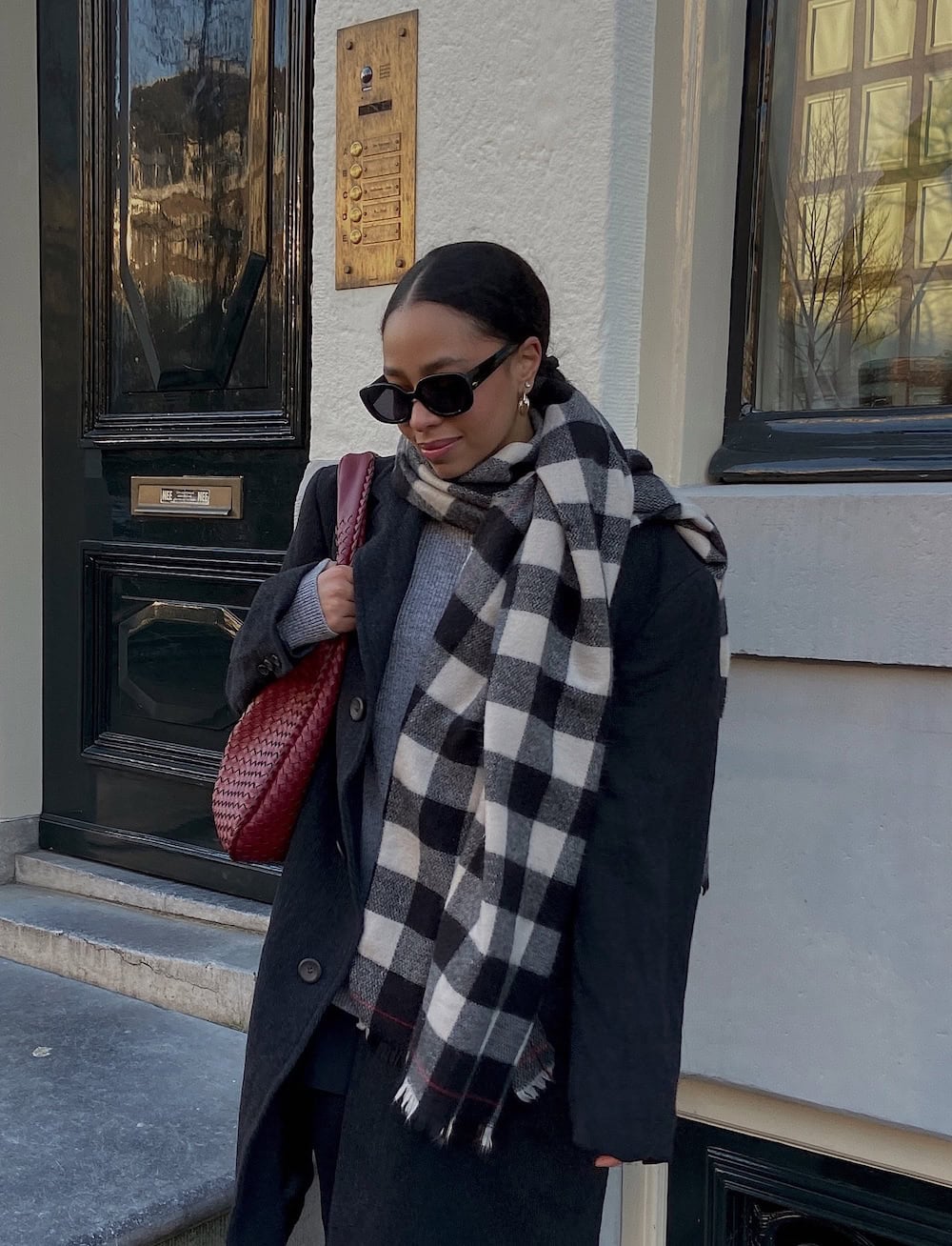 a woman wearing a grey sweater, a dark grey blazer, and a checkered scarf